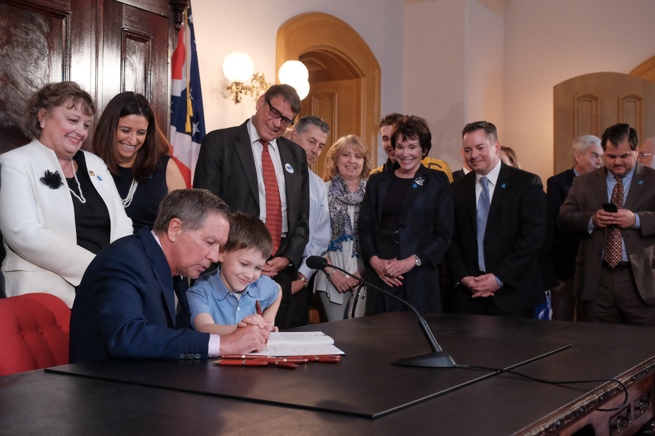 Rep. Seitz looks on as Gov. Kasich signs House Bill 463 which requires most private health insurance policies to include coverage for autism spectrum disorders on April 12, 2017.
